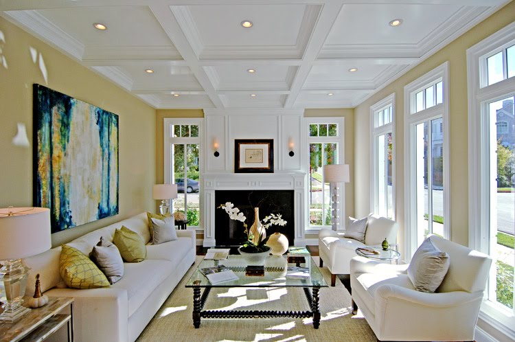 Living room by Meridith Baer with white coffered ceiling, white fireplace with decorative molding and paneling, tall windows, a long white sofa, white armchairs and modern art on the walls