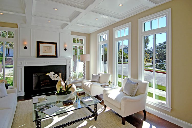 Living room by Meridith Baer with white coffered ceiling, white fireplace with decorative molding and paneling, tall windows, a long white sofa, white armchairs and modern art on the walls