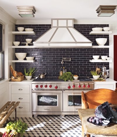 Kitchen with a Wolf range, a custom hood, black subway tile backsplash, white floating shelves and white and grey prism mosaic tile floor