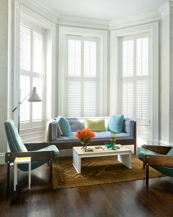 Seating area with tall bay windows with plantation shutters, wood framed settee and armchairs upholstered in shades of light blue