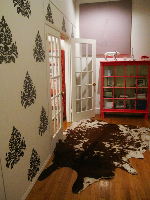 Entry way outside a nursery with dark grey medallion brocade wall decals, a hot pink glass cabinet, and a cowhide rug
