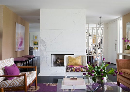 Modern living room with white marble fireplace and purple rugs, accent pillows, flowers and art
