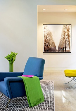 Living room vignette with bright blue armchair, electric green throw and yellow Barcelona bench in an neutral room