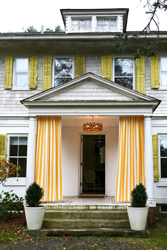 White shingled house with yellow trim and yellow and white drapery panels