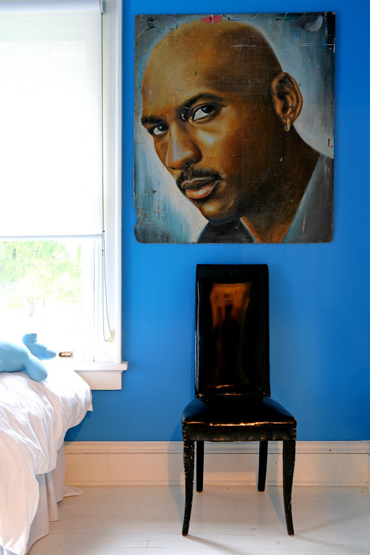 Blue bedroom by Robert and Cortney Novogratz with a black patent chair with a high back under a painting of Michael Jordan