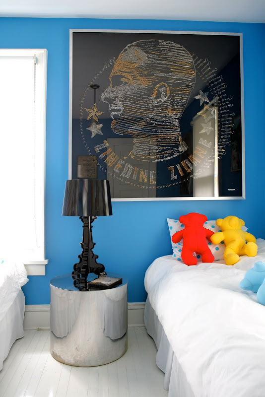 Blue room by Robert and Cortney Novogratz with a round silver side table, black lacquer lamp and a large black portrait