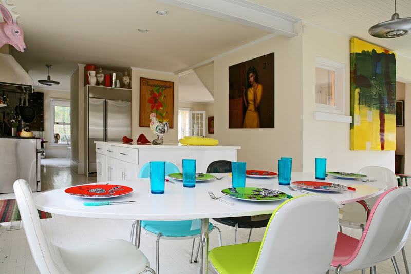 Casual dining room by Robert and Cortney Novogratz with large white oval dining table and colorful chairs, plates and glasses