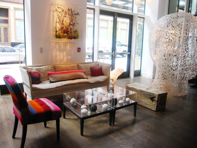 Chair with a curved back and spindle legs upholstered in a serape and an eclectic mix of furniture and a steel sculpture of a head made of letters by Jaume Plensa in the Crosby Street Hotel Lobby