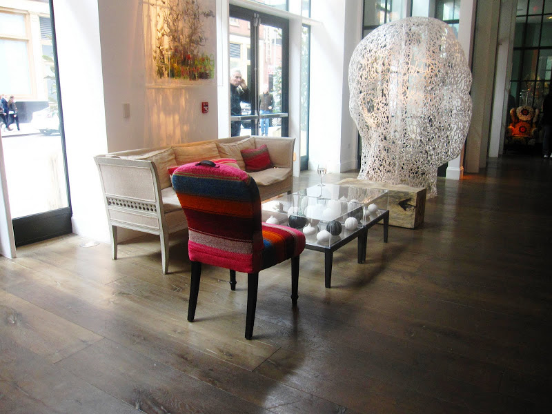 Chair with a curved back and spindle legs upholstered in a serape and an eclectic mix of furniture and a steel sculpture of a head made of letters by Jaume Plensa in the Crosby Street Hotel Lobby