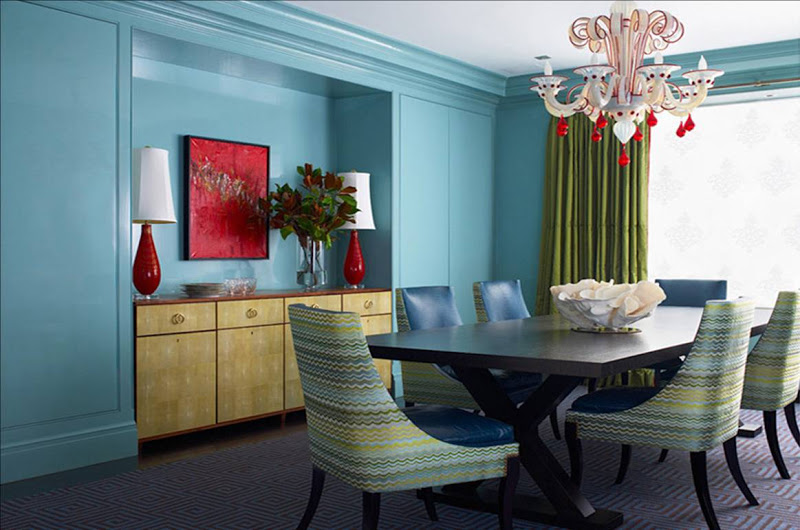 Blue dining room with a white and red glass chandelier, green curtains, and multicolored Missoni-esque upholstered dining chairs 