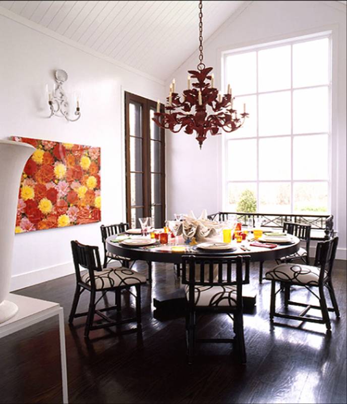 Dark dining room with iron tole red chandelier, large round table, dining chairs upholstered in black and white print and a bold and colorful floral painting