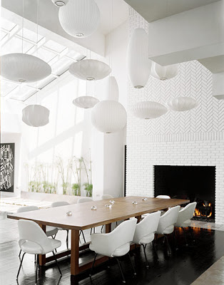 12 Nelson bubble suspension lights in different shapes and sizes hang over a modern dining room table with white Saarinen arm chairs and side chairs