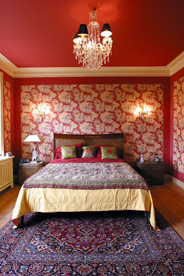 Red bedroom with graphic wallpaper, white crown molding, crystal chandelier and a Turkish rug
