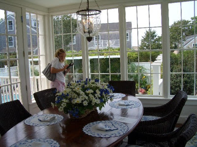 Sun room in a Nantucket home with large oval dining room table, rattan chairs and a hurricane lamp chandelier