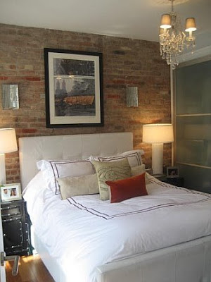 Bedroom after remodeling with exposed brick walls, upholstered headboard and white linens with red embroidery