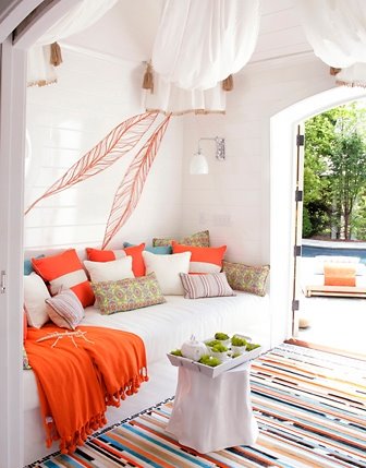 Indoor room with white sofa, orange and blue accent pillows, an orange throw and a white table