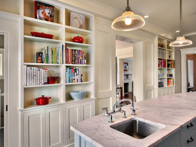 Kitchen with built in bookshelves and an island with marble counter top and light blue drawers