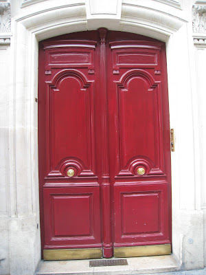 A rich red door with curved top, detailed panelling and shiny brass knobs and trim on Rue de Thorigny