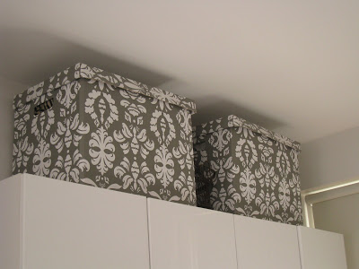 Brocade print storage boxes on top of white cabinets in a London kitchen
