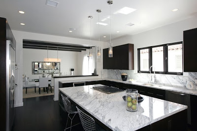 Black and white kitchen with a huge island with marble counter top, dark wood cabinets and drawers and stainless appliances