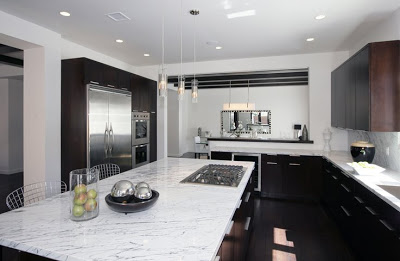 Black and white kitchen with a huge island with marble counter top, dark wood cabinets and drawers and stainless appliances