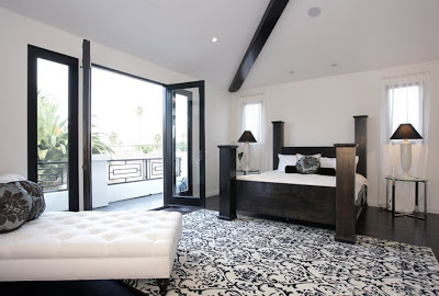 Black and white master bedroom with double French doors opening to a balcony, a Moroccan print rug and a large black four poster bed