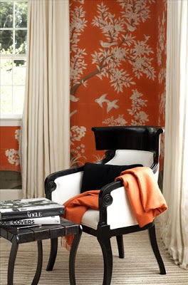 Bedroom with a corner reading are with a black armchair with white upholstery and an orange throw