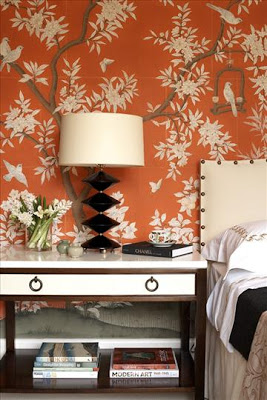 Bedroom with orange wallpaper with a blossoming tree and a nightstand with a black lacquer lamp