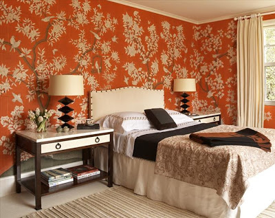 Bedroom with orange wallpaper with a blossoming tree, white headboard with nail head trim and a dark wood nightstand with white drawer and top