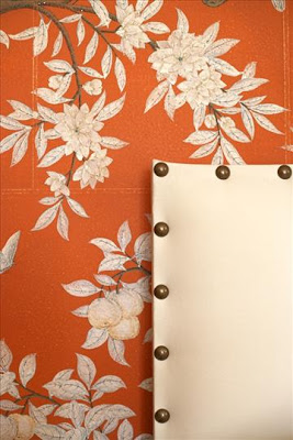 Bedroom with orange wallpaper with a blossoming tree and an off-white upholstered headboard with nail head trim