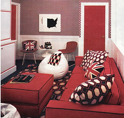 Den with a red sofa and ottoman with black piping, white bean bags, white wainscoting, red doors, and graphic print wallpaper, throw pillows and rug