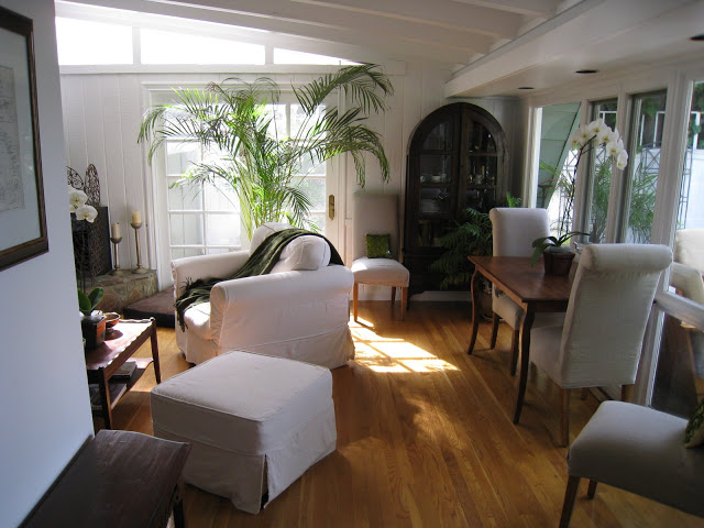 Small living room with white armchair, wood floor, high back grey upholstered chairs around a traditional table and French doors