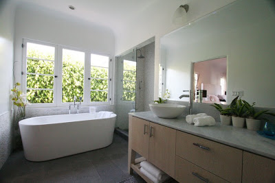 Master bathroom with free standing tub surrounded by windows, light wood cabinets and grey tiled slate floors