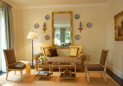 Living room with a settee upholstered in Greek key patterned fabric and yellow throw pillows with brown trim, two small tables with gold legs and decorative plates on the walls by Palmer Weiss