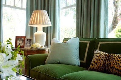 Classic living room with a green sofa with back pillows with white border, a wood side table with a white table lamp and a leopard print accent pillow