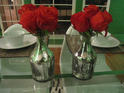 Two silver bud vases with red roses on a dining room table