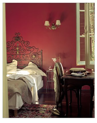 Bedroom with red walls, wrought iron scroll headboard and dark wood desk with matching chair
