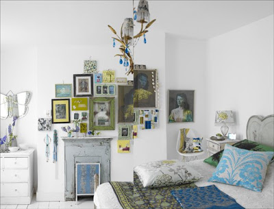 White bedroom with blue and green accents and a collage of framed pictures on a fireplace mantel