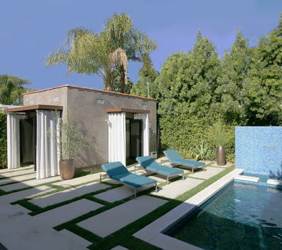 Backyard with a pool surrounded by cement pavers and furnished with modern blue chaise lounge chair. The garage has been transformed into an open air pool house