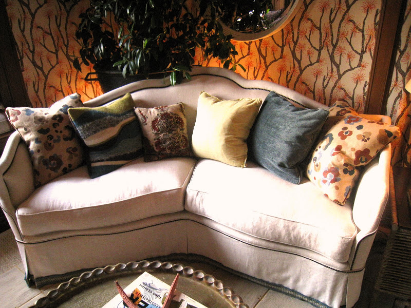 Array of pillows on a curved cream love seat in a sitting room designed by Lucas Studio, Inc in the Greystone Mansion