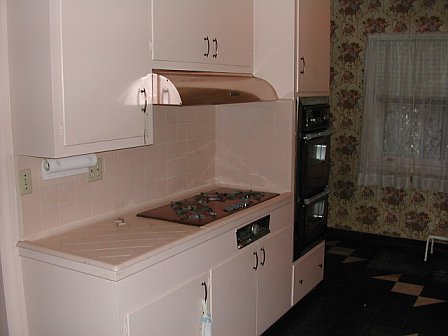 Pink kitchen with a copper stove top and hood, black ovens and floral wallpaper before remodeling by Newman & Wolen Design