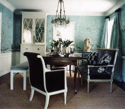 Dining room with light blue floral wallpaper, a dark brown upholstered armchair with white legs and arms and nail head trim, a white lacquer cabinet with mirrored doors, a white Chippendale bench upholstered in light blue velvet and an upholstered and wood settee by Windsor Smith