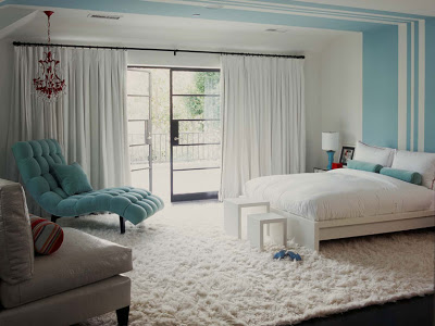 Turquoise bedroom with painted stripe headboard, tufted blue chaise lounge, bolster neck pillows and a matching side lamp