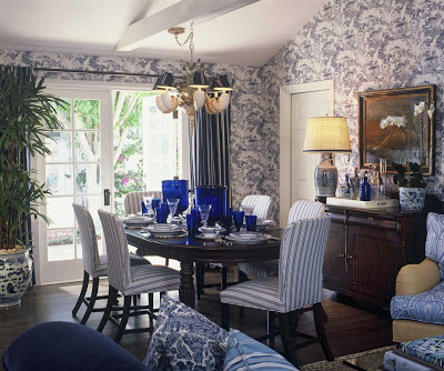 Traditional dining room with blue tolie wallpaper, upholstered blue and white striped dining chairs, Asian inspired blue and white ceramic lamp and garden stool by Barclay Butera