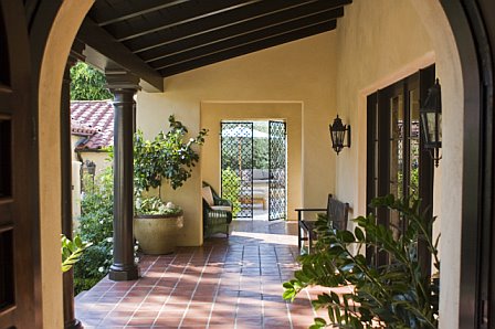 Los Angeles home after remodeling with a Spanish tiled covered walkway with columns, arches and beams leading from the front door to an ornate iron gate that opens onto a patio and pool area