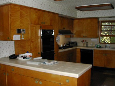 Kitchen before remodeling with honey colored wood cabinets and floral wallpaper