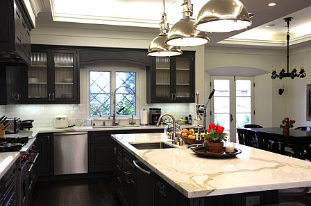 Kitchen after remodeling with Calcutta Gold marble countertops, dark brown painted wood cabinets, new windows, subway tile backsplash and pendant kitchen island lighting