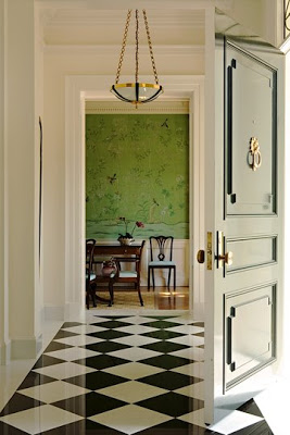 Entryway by Los Angeles interior designer Elizabeth Dinkel with black and white checkerboard floor, hunter green door with paneling, molding and a simple brass pedant