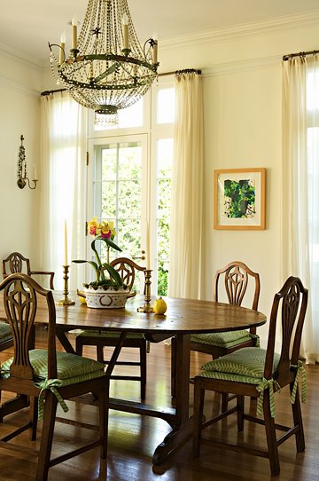 Traditional dining room with a large crystal chandelier, dark stained wood table, Queen Anne chairs with green cushions and off white walls