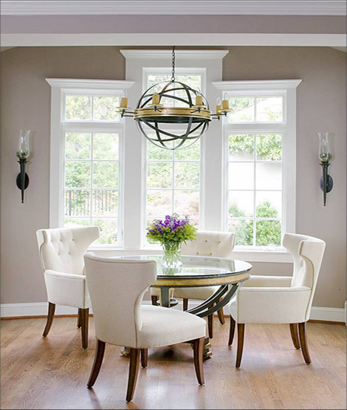 Dining room with grey walls, round glass table with a metal base, white tufted wingback chairs. simple wall scones and metal orb chandelier